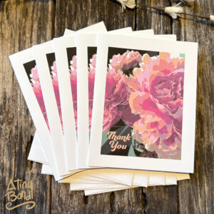 Thank You note cards with a close up of pastel peony flowers, and white envelopes, on a distressed wood background.